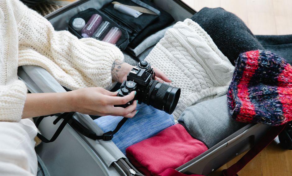 A person packing sweaters and a camera in a suitcase, preparing for travel.